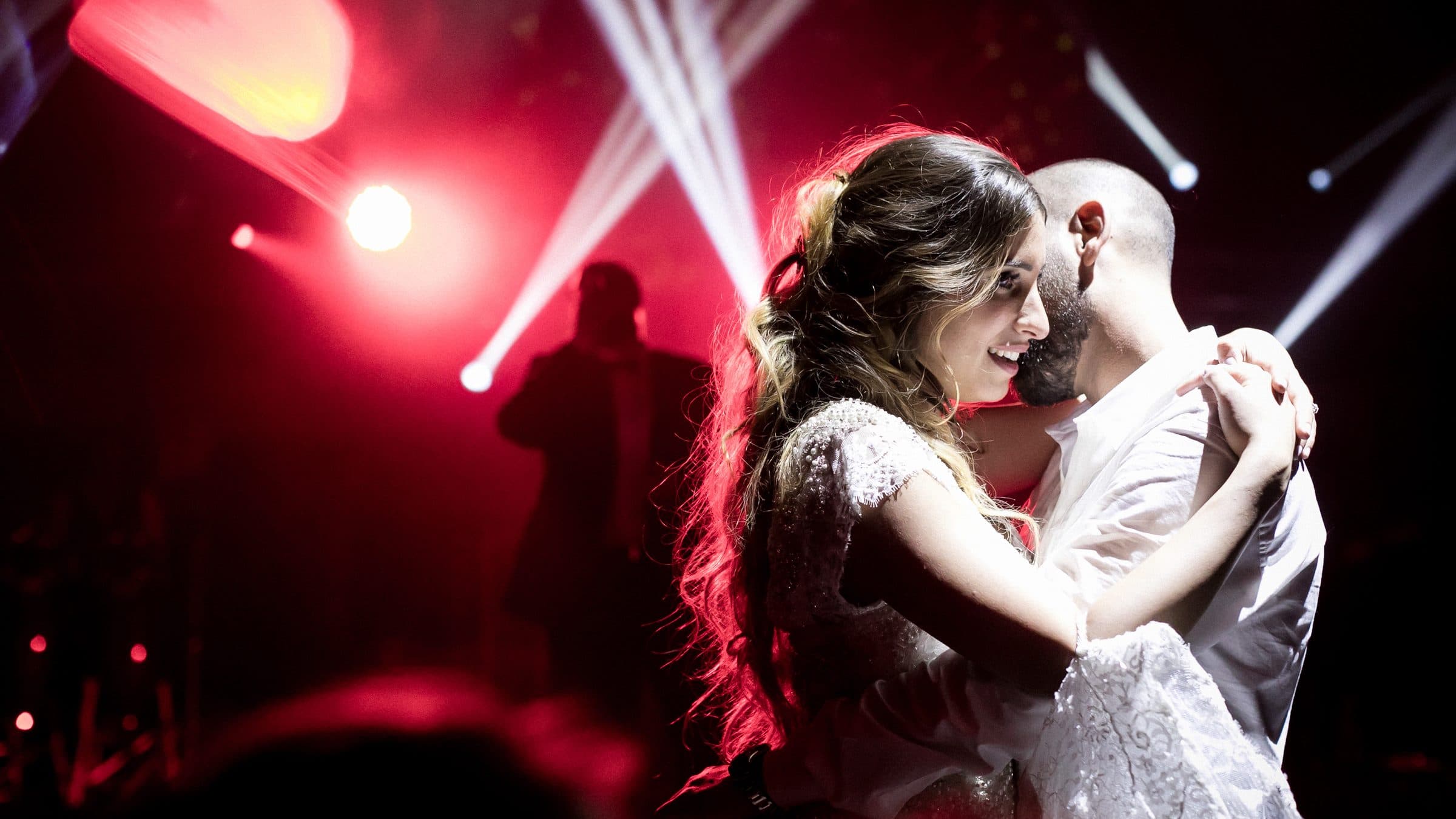 Les mariés enlacés pendant leur première danse, sous des faisceaux rouges et blancs